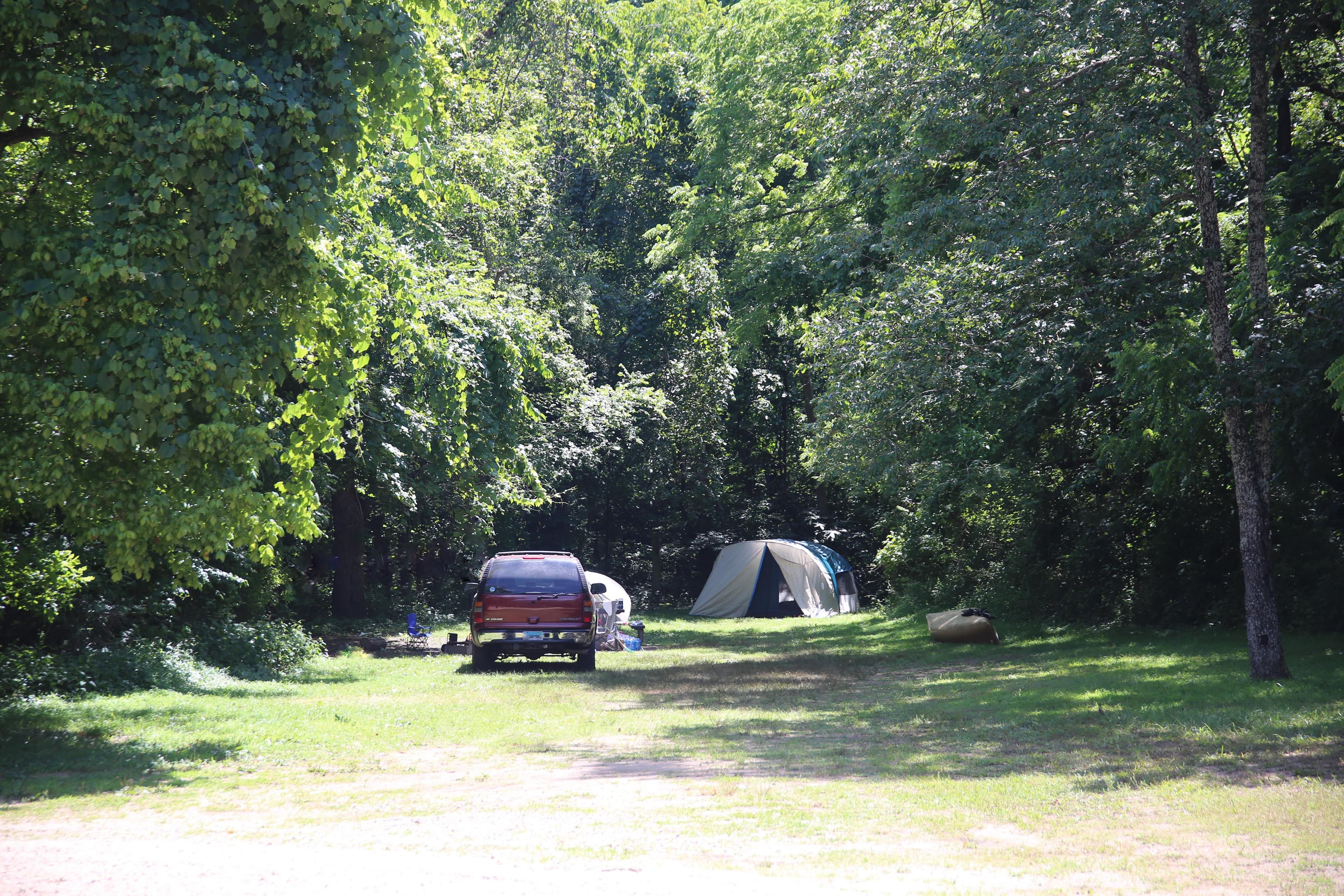 A car and tent occupy a campsite surrounded by trees.