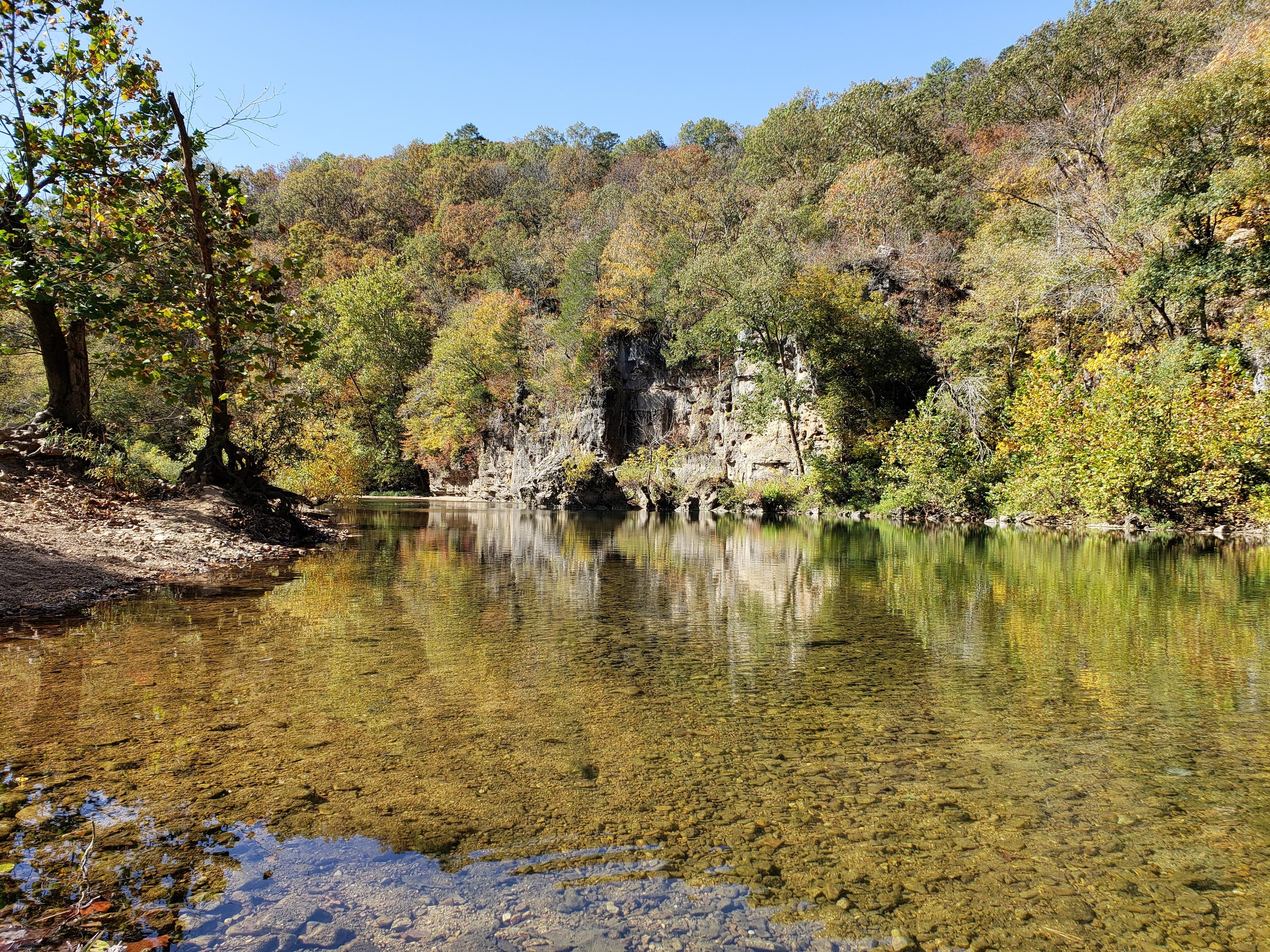 A large bluff stands over a cluster of boulders. Clear waters flow from the area.